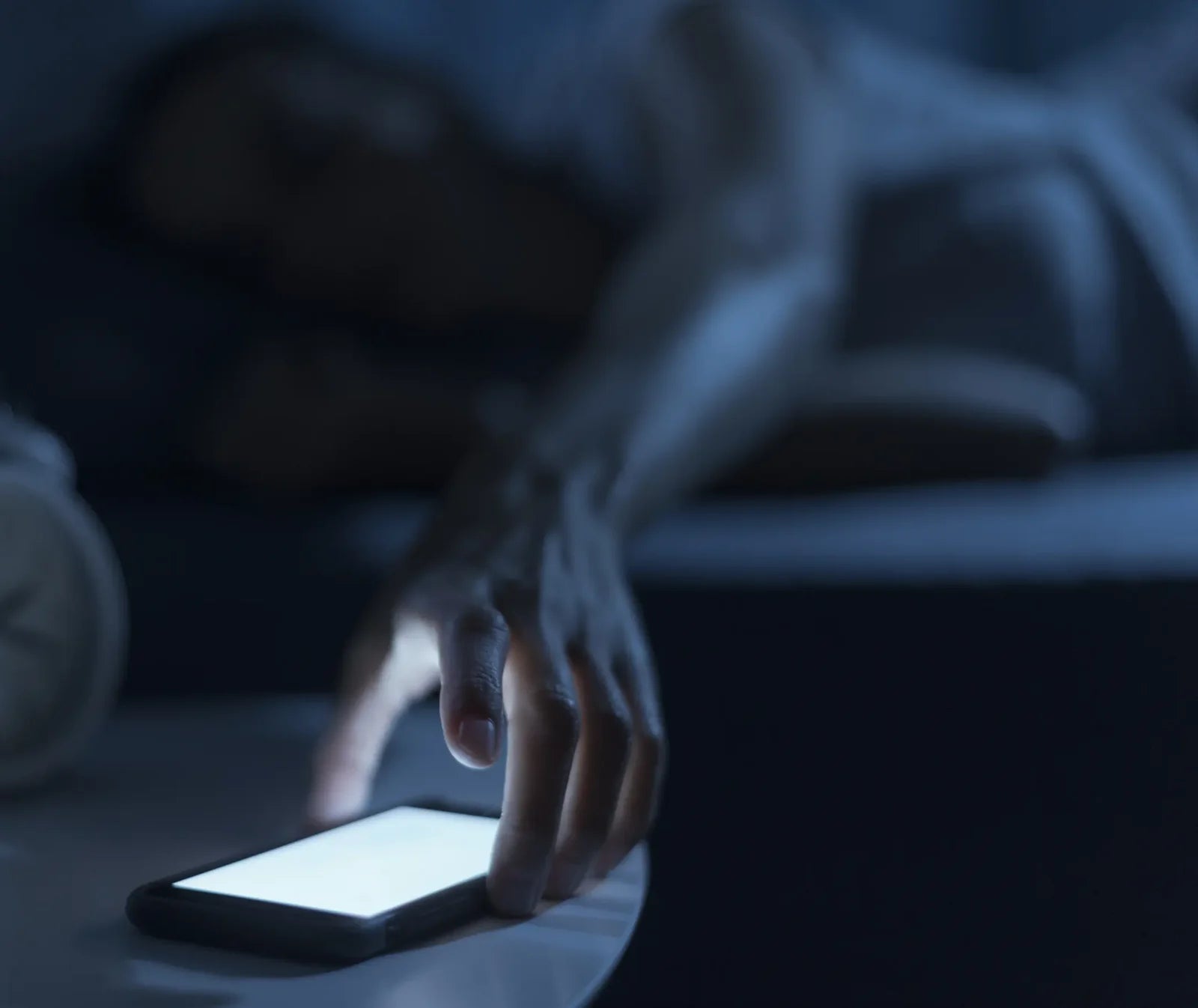 Ranka tamsoje siekia telefono ant naktinio staliuko